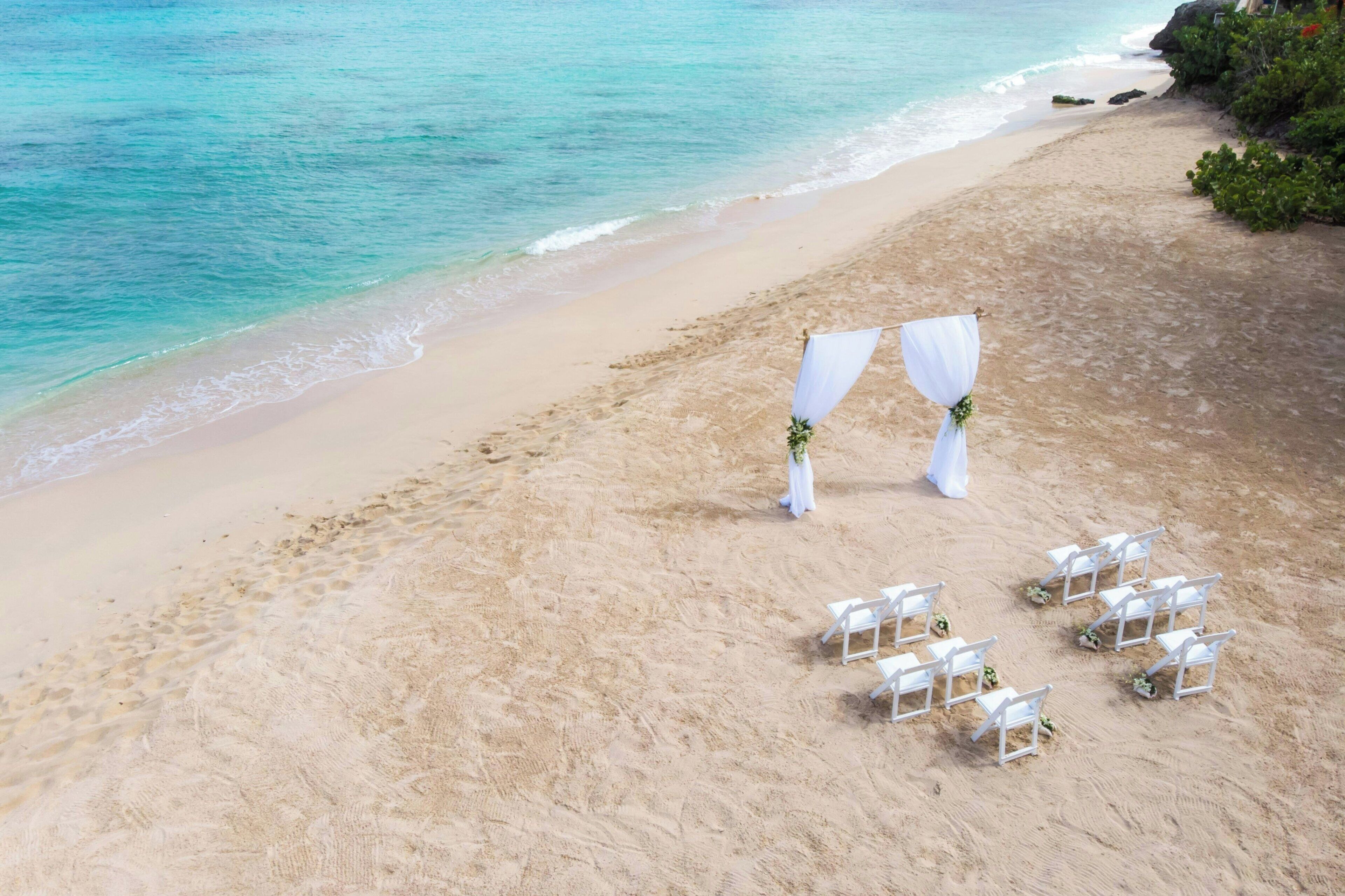 Een bruiloftdecoratie op het strand, met een witte boog en stoelen.
