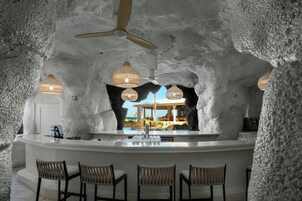 Una zona de bar con una isla central, taburetes de bar, ventiladores de techo e iluminación colgante.