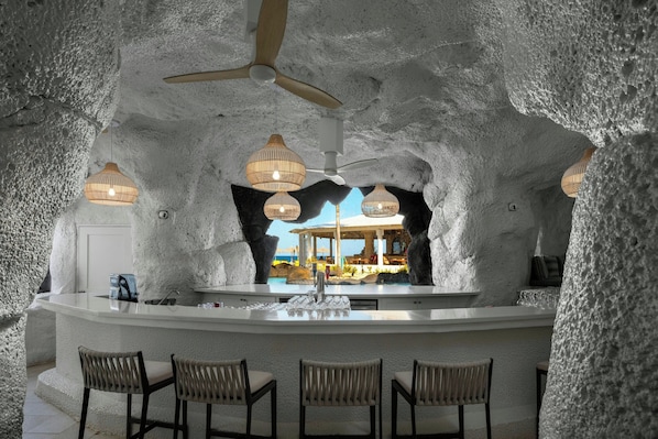 A bar area with a central island, bar stools, ceiling fans, and hanging light fixtures. - Crystal Cove, A Tribute Portfolio All-Inclusive Resort (Derricks)
