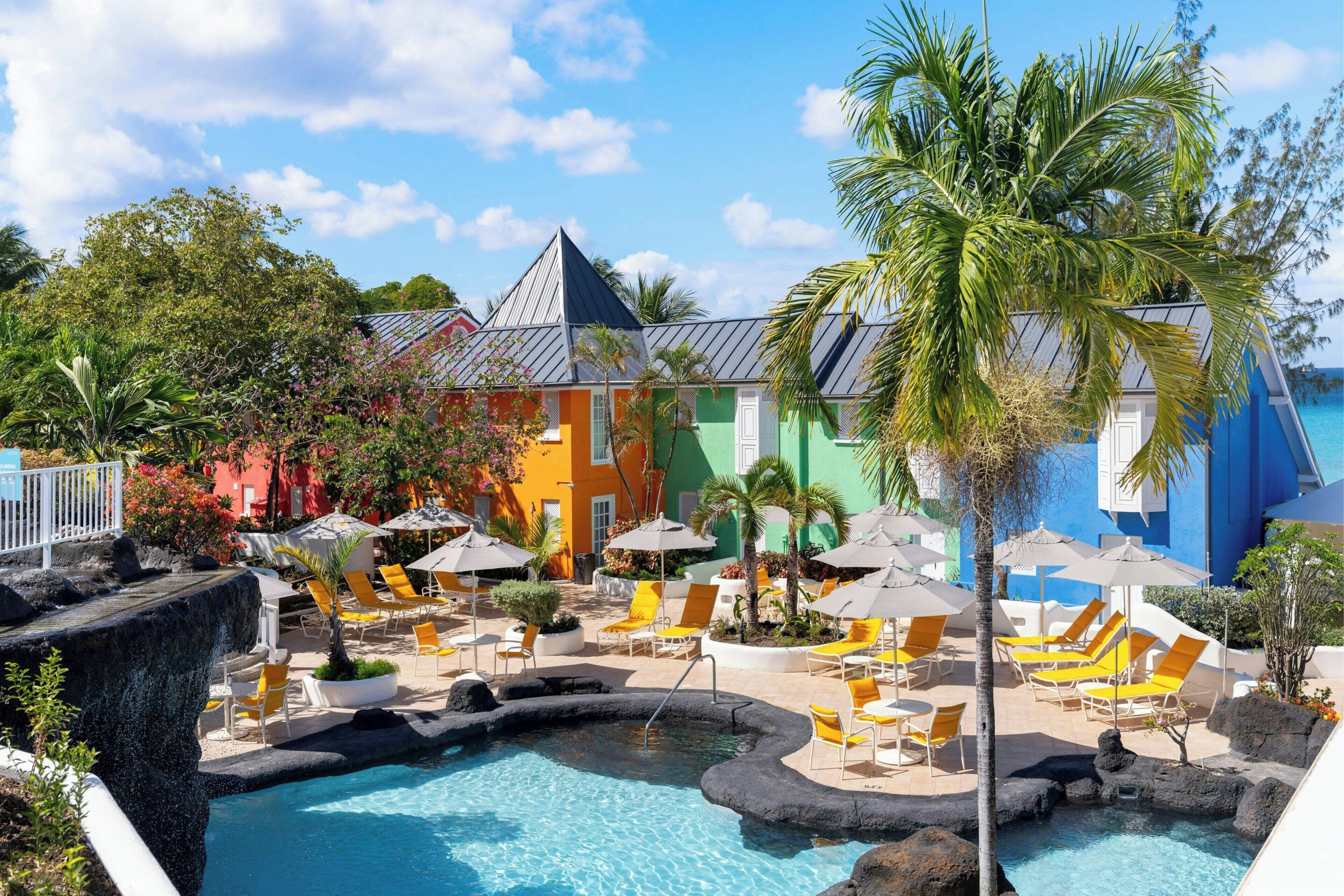 A resort with a swimming pool, lounge chairs, and colorful buildings.