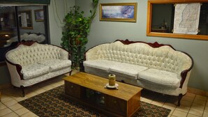 Un salon avec deux canapés blancs à capitonnage, une table basse en bois, des tapis à motifs, une grande fenêtre et une carte encadrée accrochée au mur.