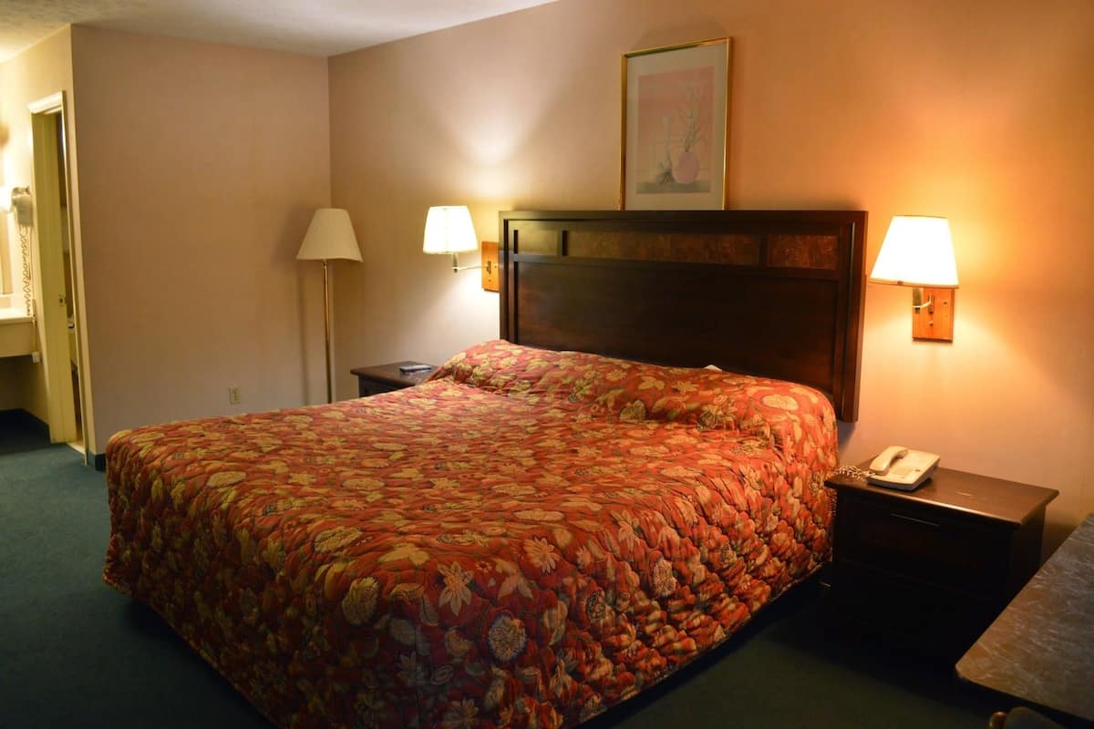 A hotel room with a large bed, two bedside lamps, a nightstand with a phone, and a framed picture on the wall.