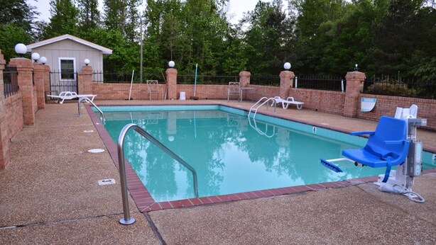 Une piscine bordée d’un mur en briques, avec des chaises longues et un petit bâtiment en arrière-plan.