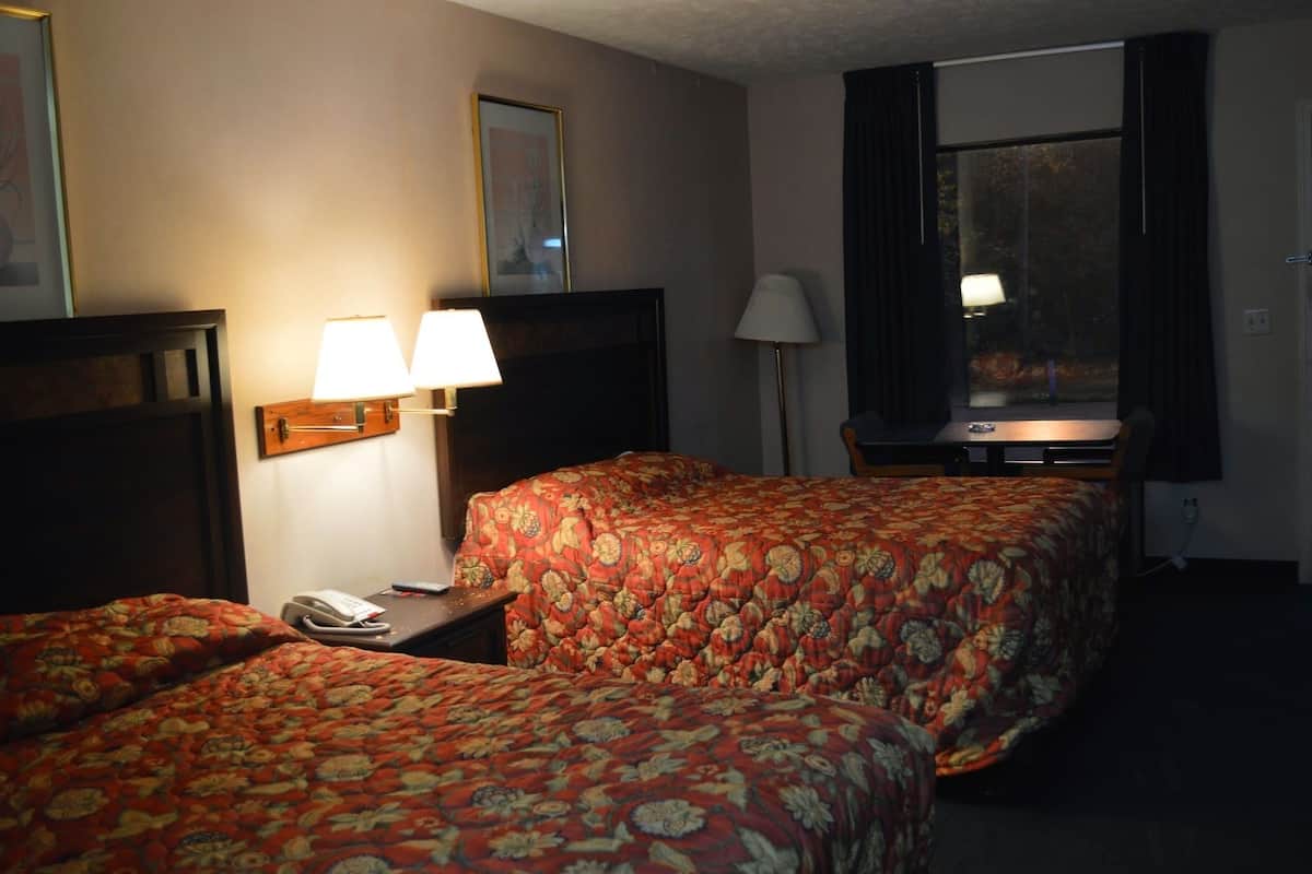 A hotel room with two beds, a desk with a lamp, a phone, and a window with curtains.