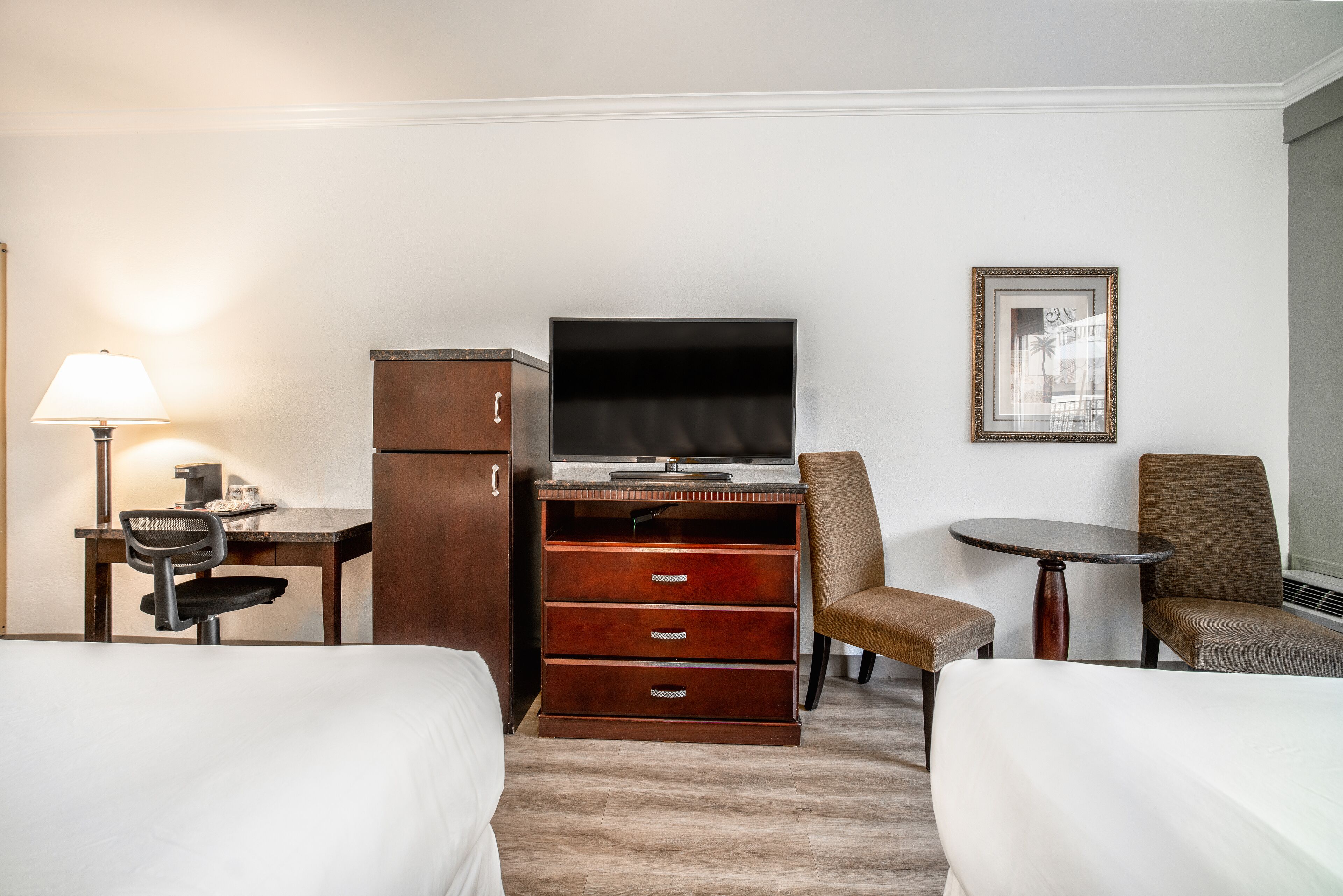 Habitación de hotel con dos camas, un escritorio con lámpara, un televisor, un aparador y dos sillas.