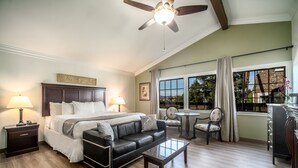 A hotel room with a bed, a leather sofa, a coffee table, a desk, and a dining area with a chair and table. - Kronborg Inn (Solvang)