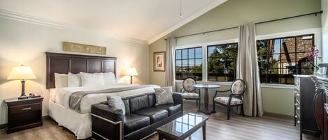 A hotel room with a bed, a leather sofa, a coffee table, a desk, and a dining area with a chair and table.
