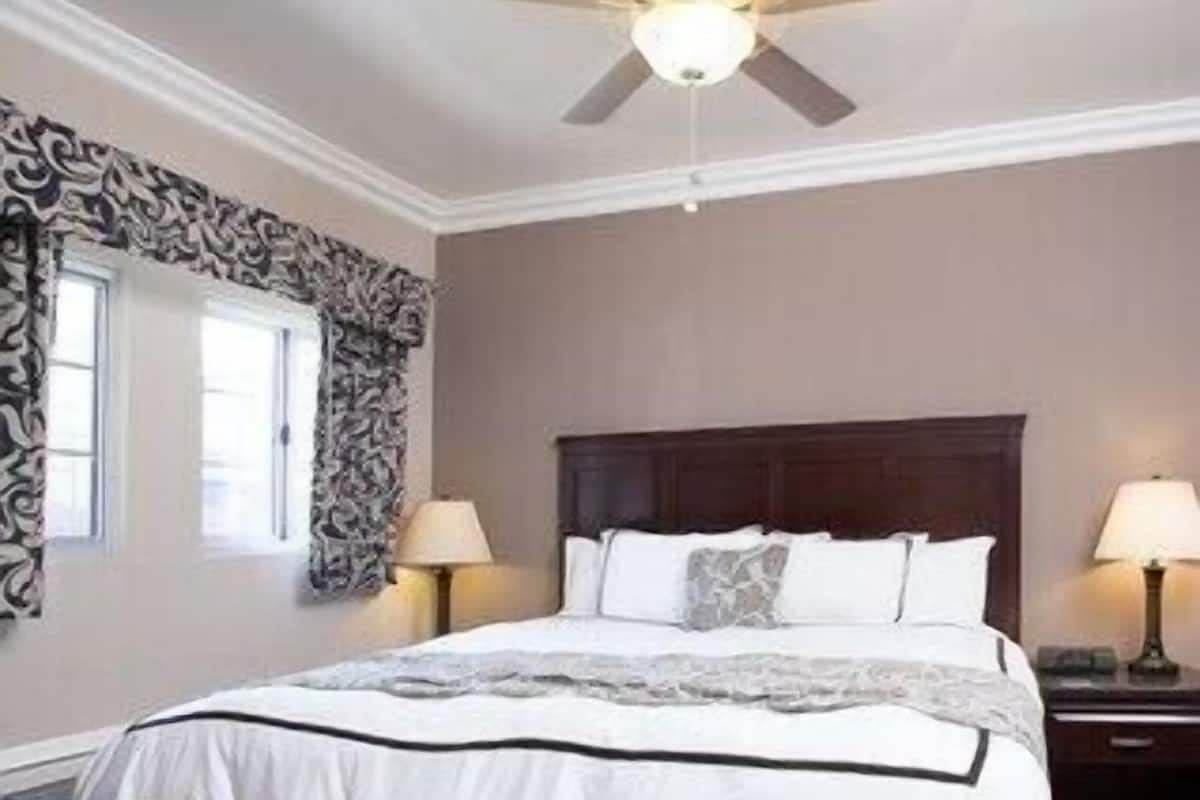A bedroom with a bed, two bedside tables, a ceiling fan, and patterned curtains.