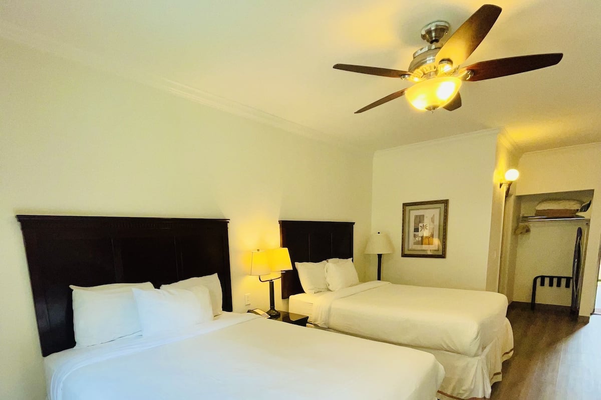 A hotel room with two beds, a ceiling fan, and a framed picture on the wall.