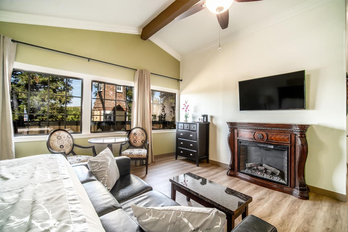 A room with a bed, a sofa, a fireplace, a television, and a dining area with a table and chairs.