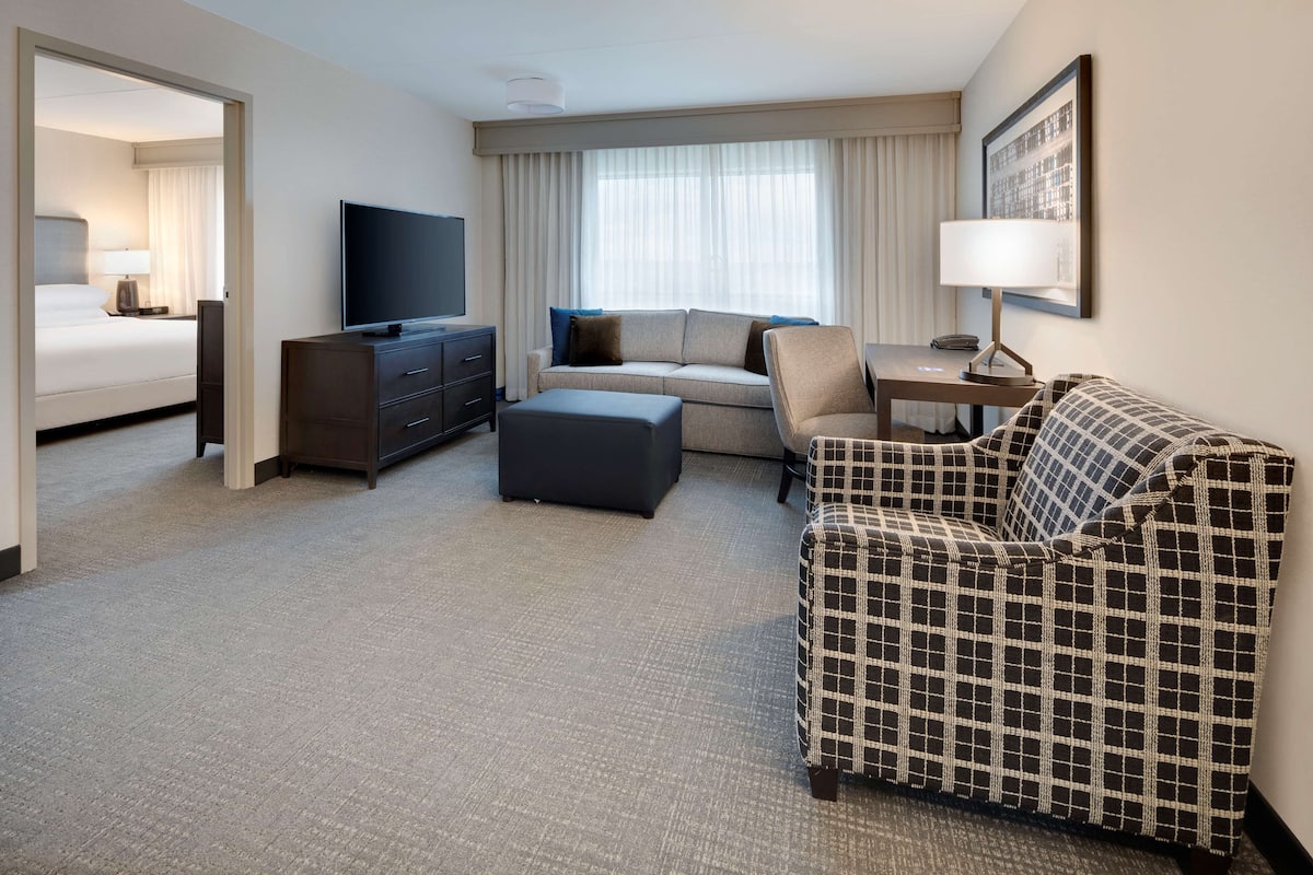 A hotel room with a bed, a sofa, a chair, a TV, a desk, and a lamp.