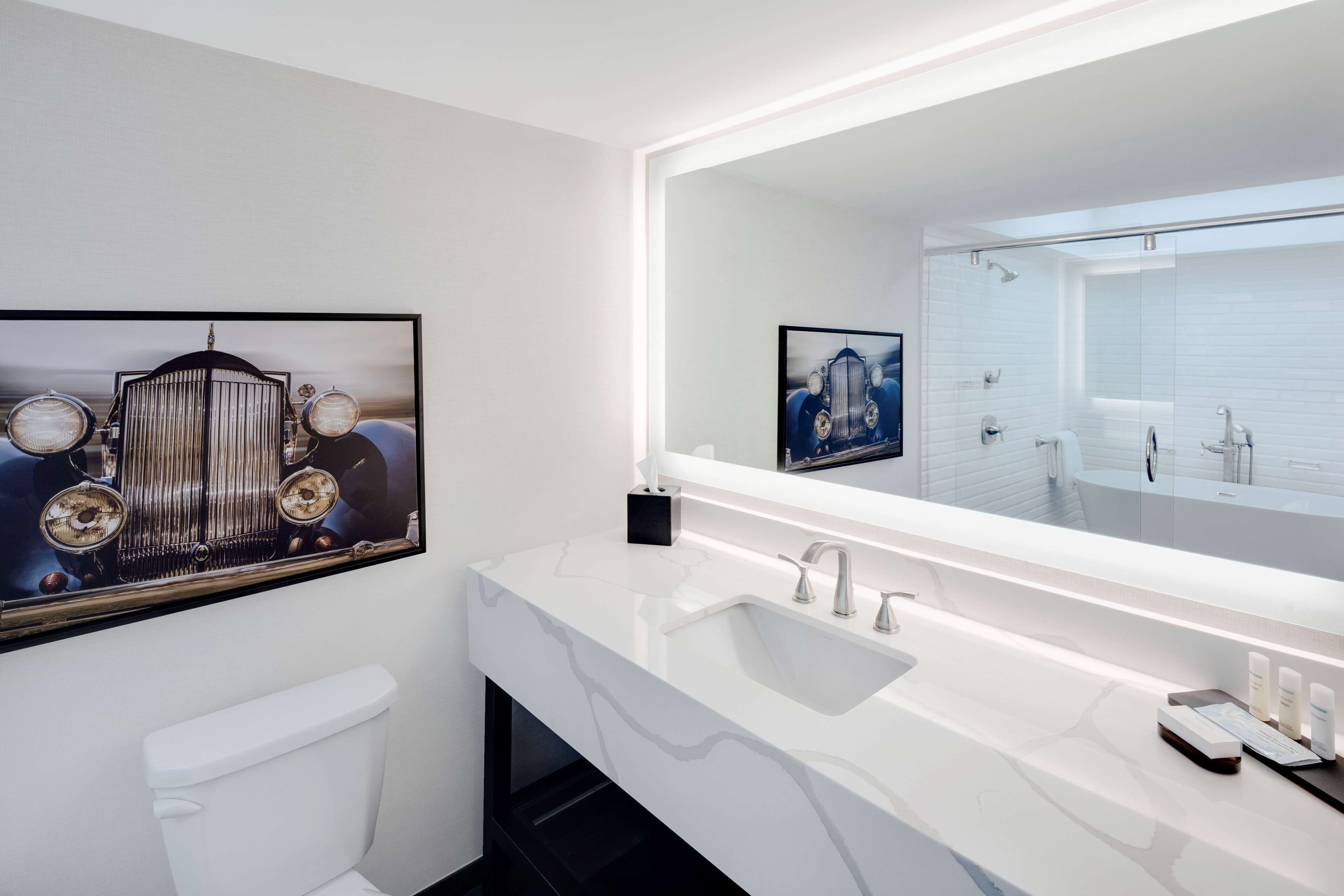Un baño moderno con un espejo grande, accesorios blancos y obras de arte en las paredes.