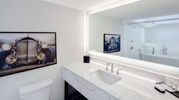 Un baño moderno con un espejo grande, accesorios blancos y obras de arte en las paredes.