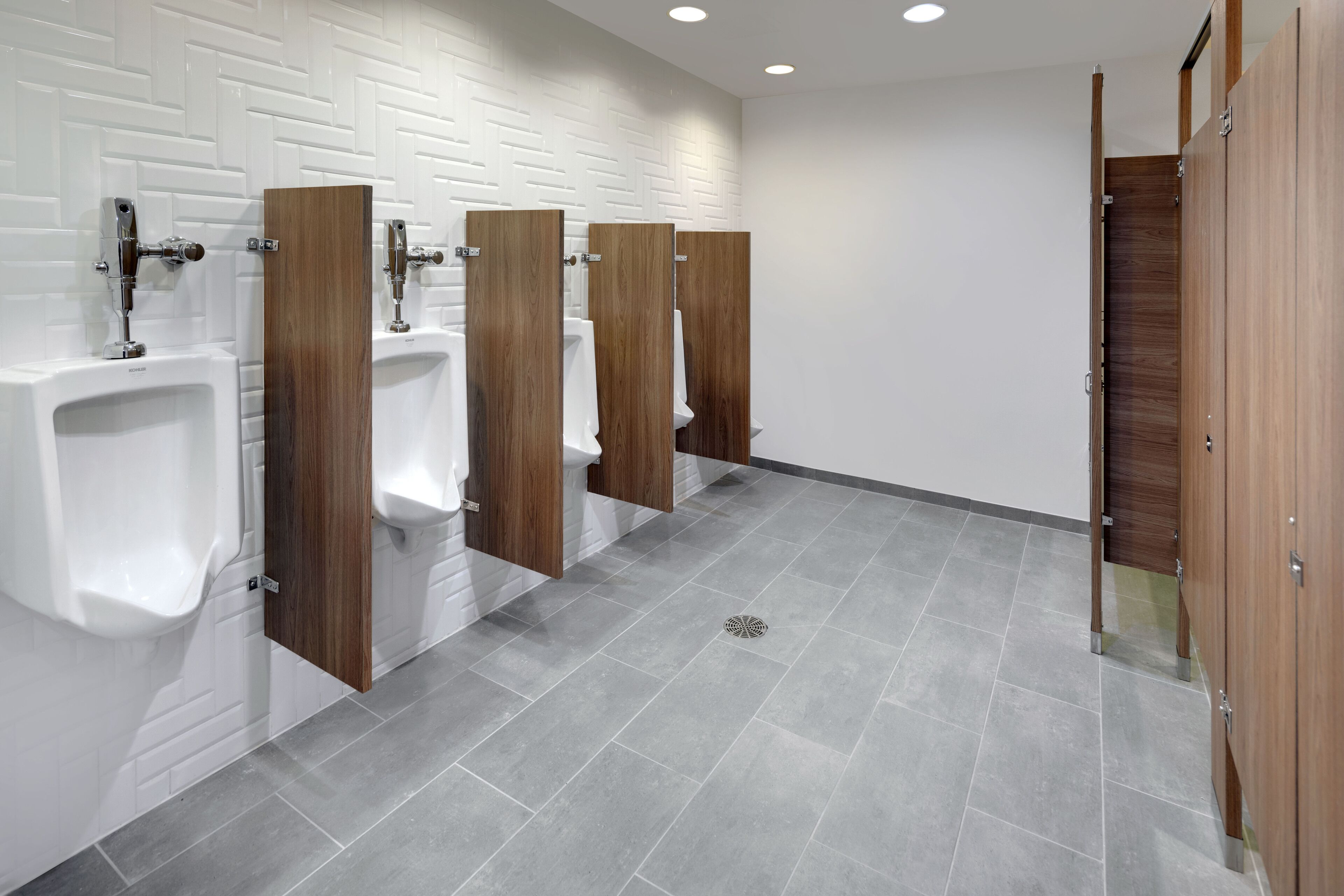 A modern restroom with white tiled walls, grey tiled floors, and wooden partitions.