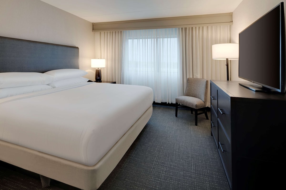 A hotel room with a large bed, a television, a chair, and a desk with drawers.