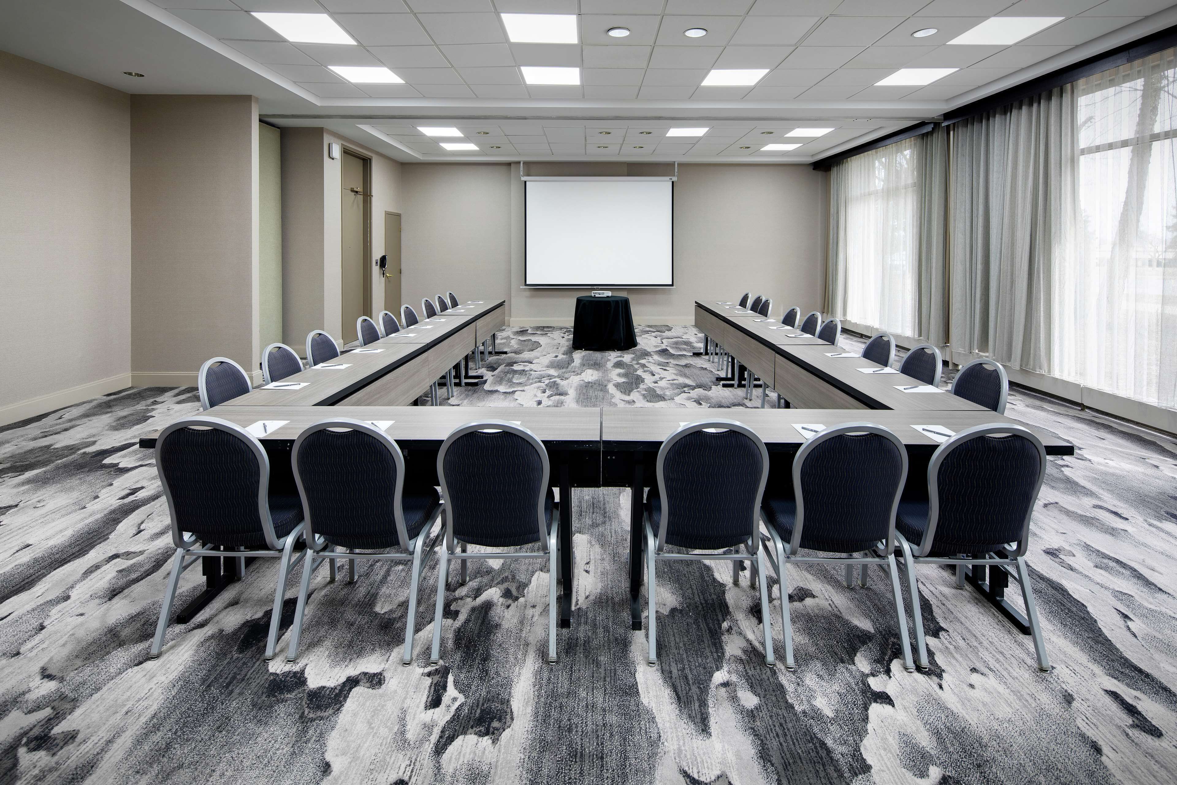 Un salón de conferencias con una larga mesa, sillas, una pantalla de proyector y piso alfombrado.