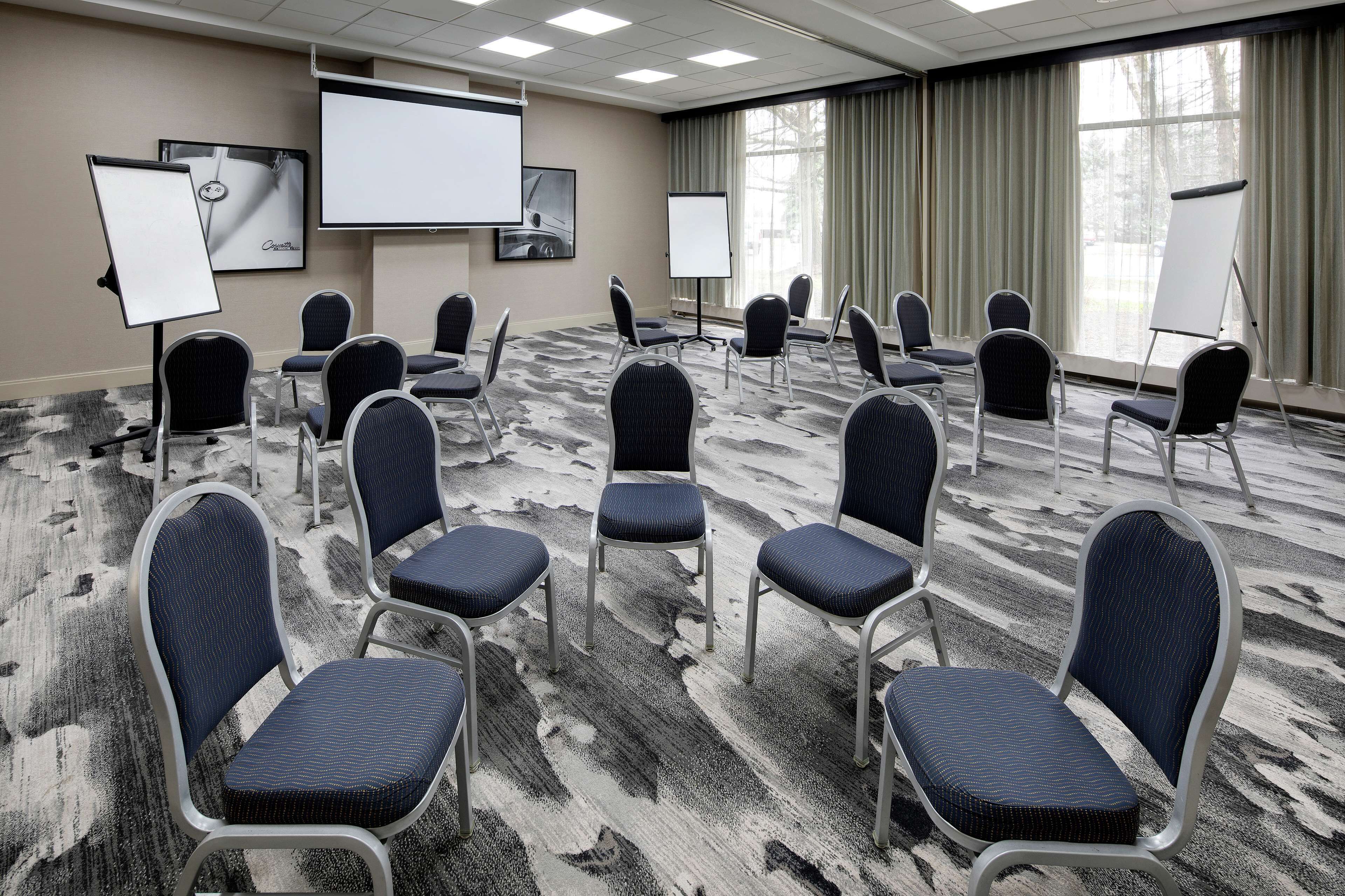 Una sala conferenze con pavimento tappezzato, numerosi posti a sedere, uno schermo per proiettore e una lavagna.