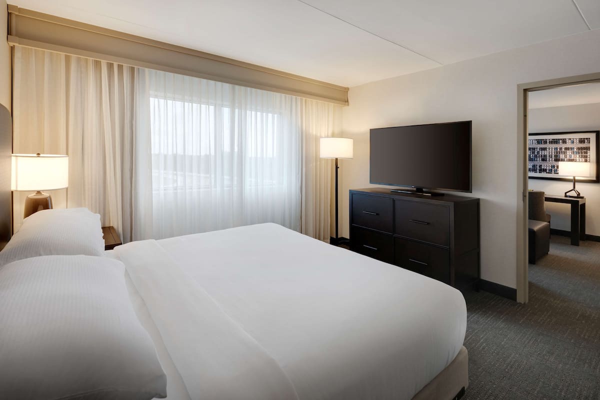 A hotel room with a large bed, a flat-screen TV, a desk with a lamp, and a framed picture on the wall.