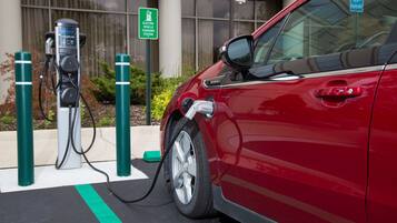 A red car connected to an electric vehicle charging station with a handicap parking sign in the background.