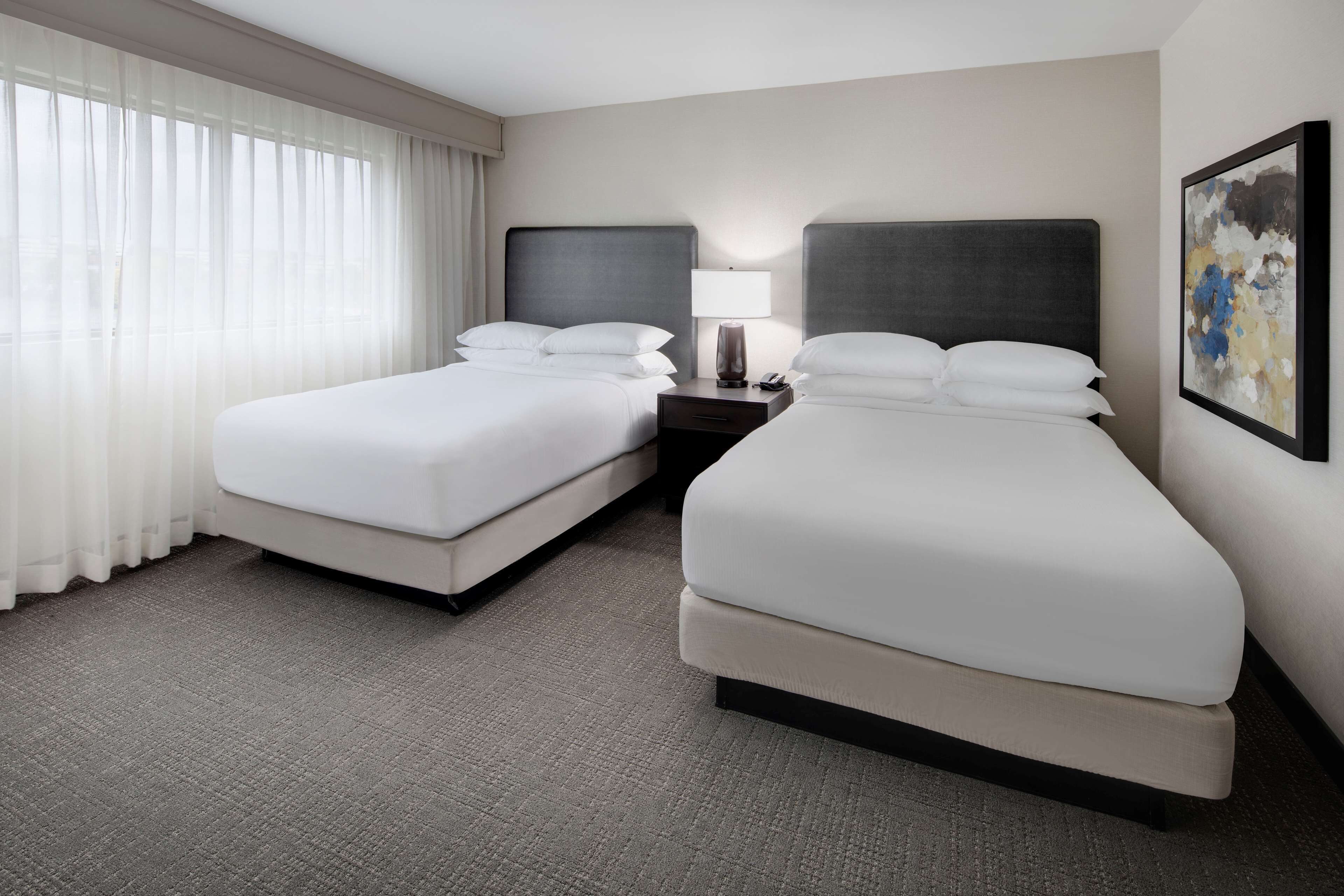A hotel room with two beds, a nightstand with a lamp, and a painting on the wall.
