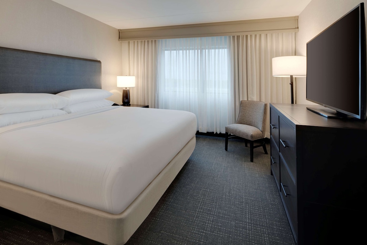 A hotel room with a large bed, a television, a chair, and a desk with drawers.