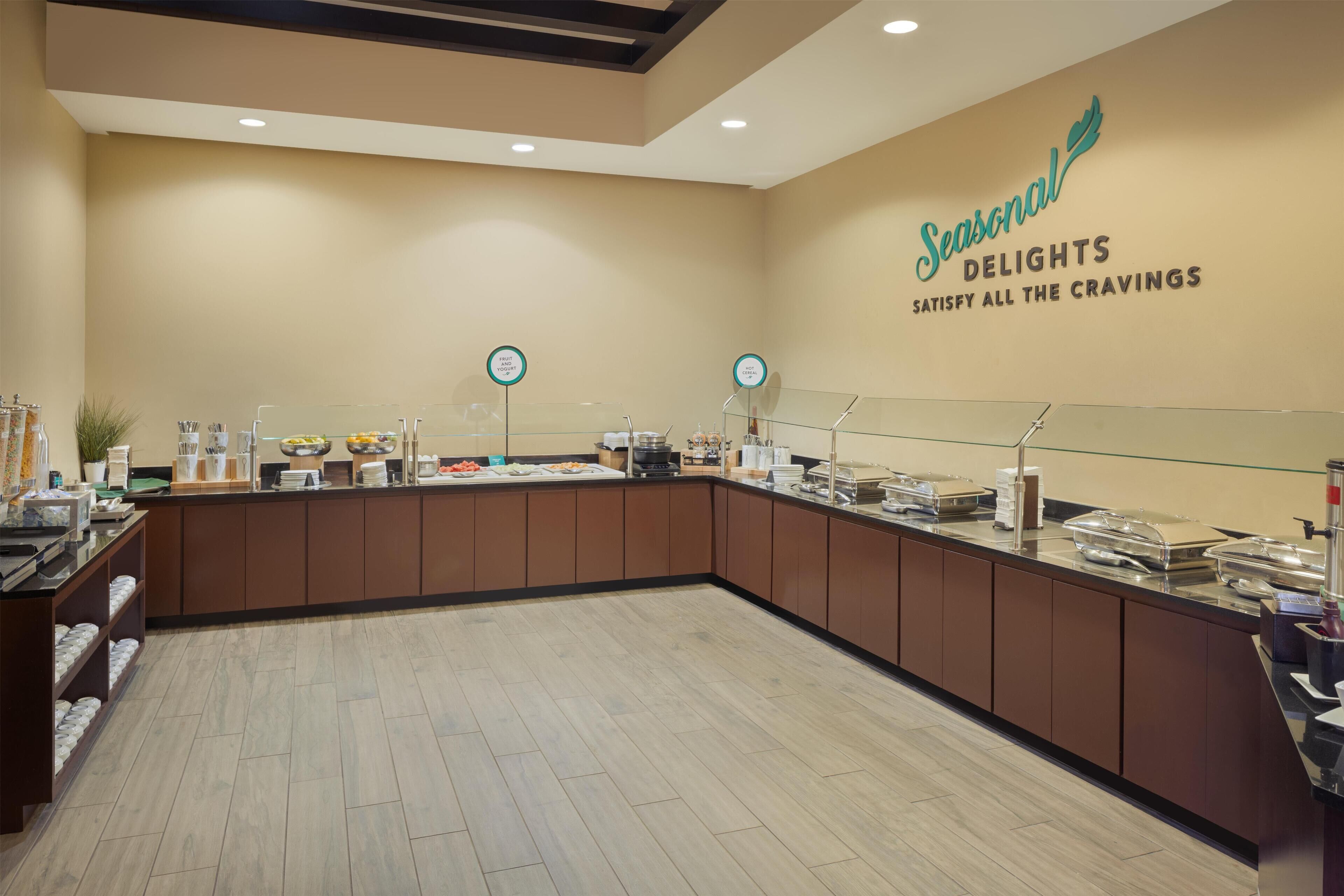 Un espace buffet comprenant un comptoir, un présentoir pour les plats et une enseigne murale indiquant : « Les saveurs de saison, pour satisfaire toutes vos envies ».