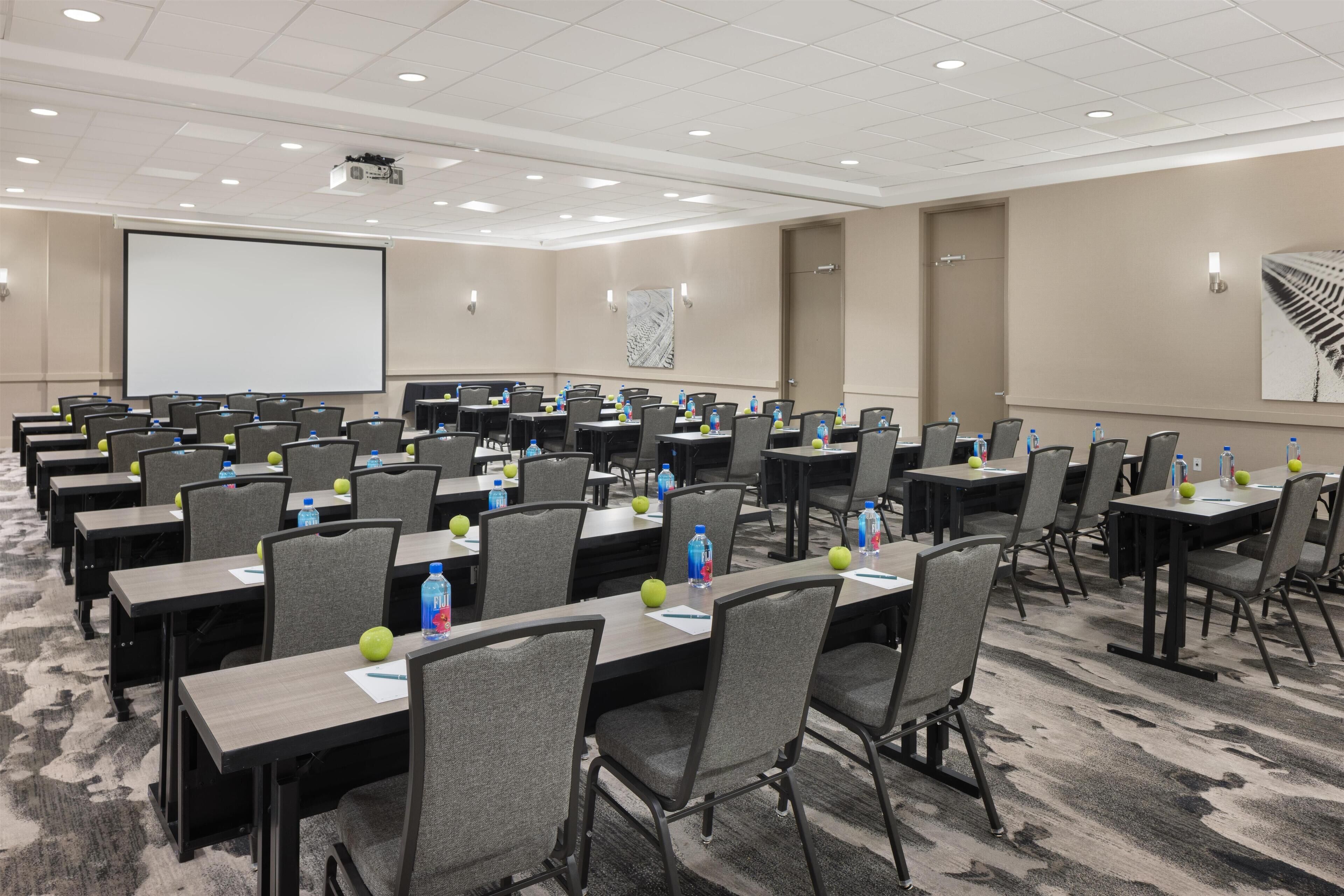 A conference room with multiple tables and chairs, equipped with water bottles and notepads.