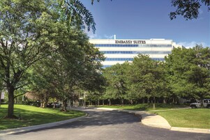 Un edificio con el letrero "Embassy Suites", con una entrada de acceso en curva y árboles circundantes.