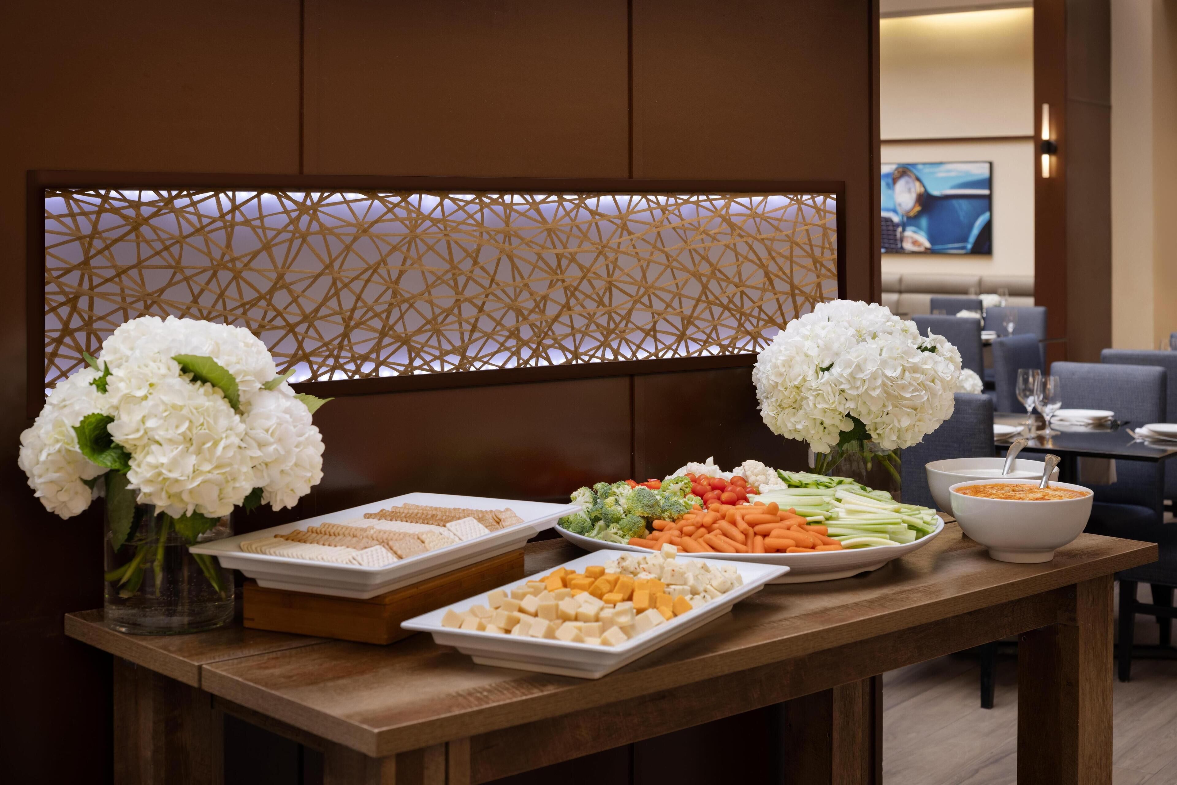 A buffet table with various food items and two vases of white flowers.