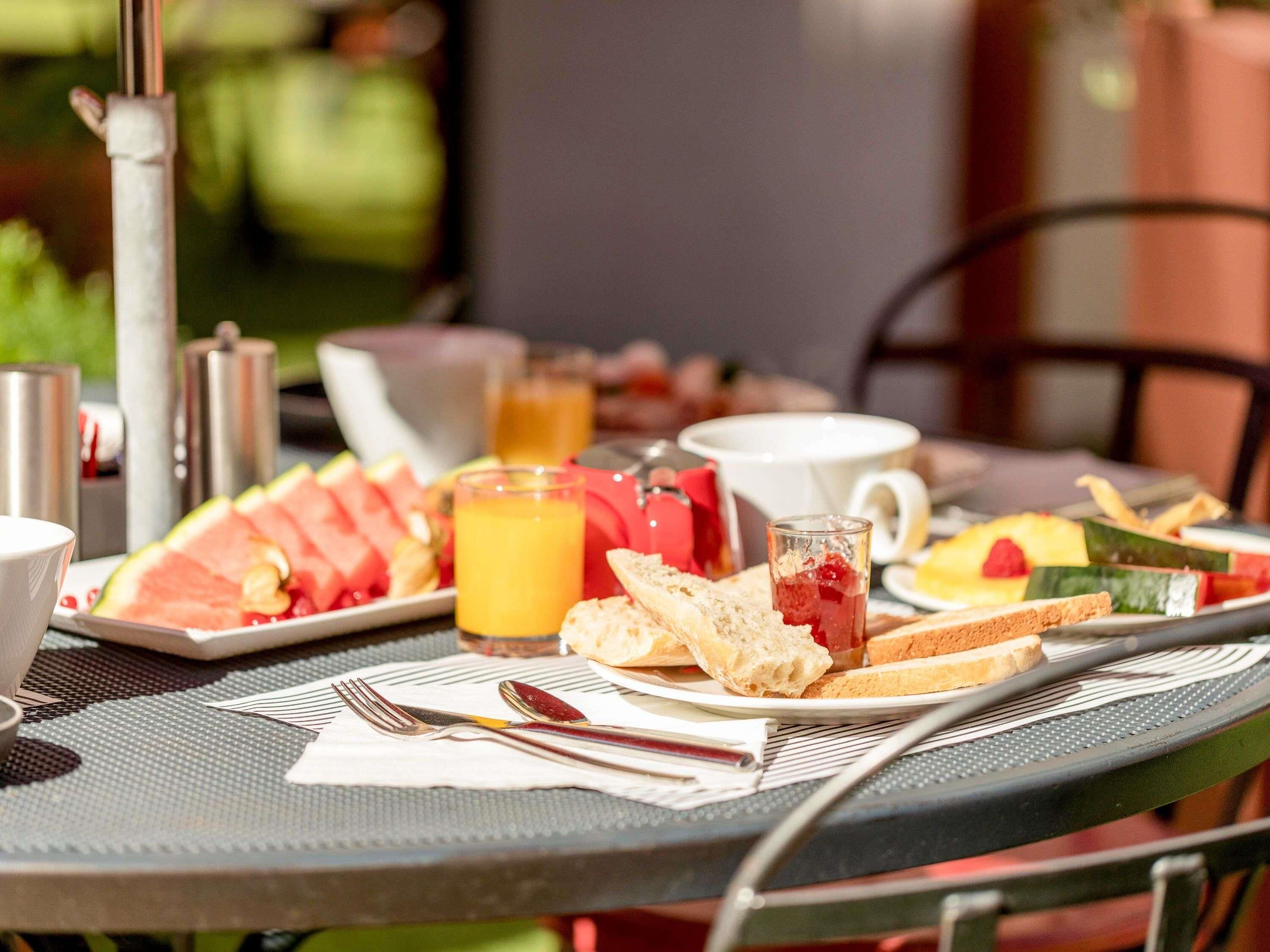Mesa de café da manhã com pratos de comida, um copo de suco de laranja e uma xícara.