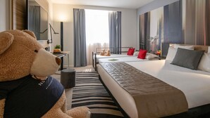 A hotel room with a large bed, a desk, a chair, a teddy bear, and a large window with curtains. - Novotel Nice Centre Vieux Nice (Nice)