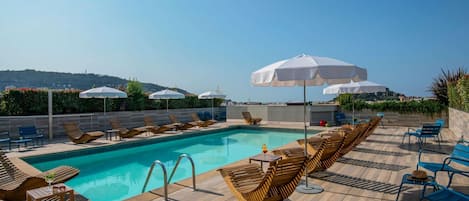 Una piscina al aire libre, sombrillas, sillones reclinables de piscina