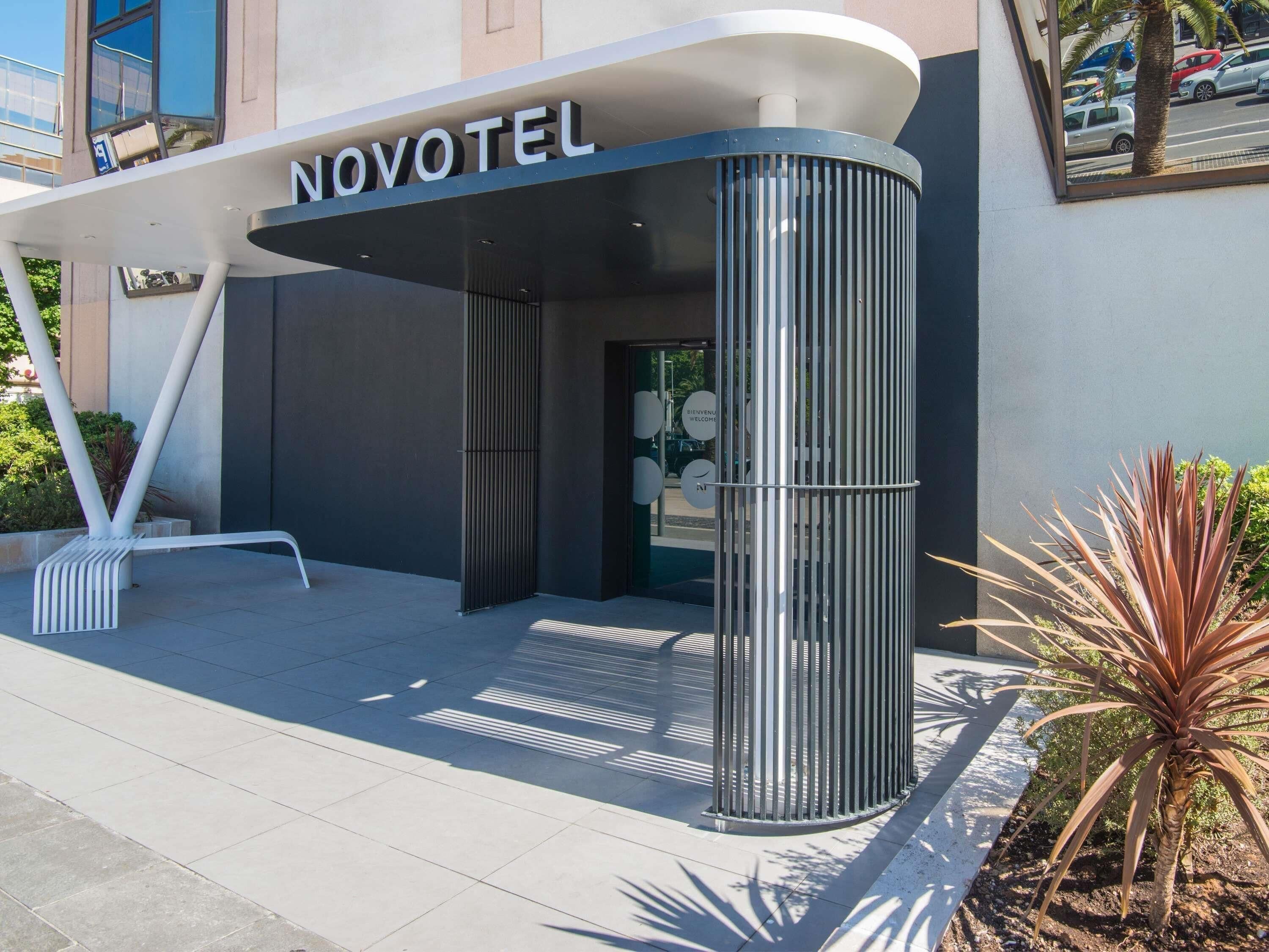 A modern hotel entrance with a curved facade, a metal column, and a bench outside.