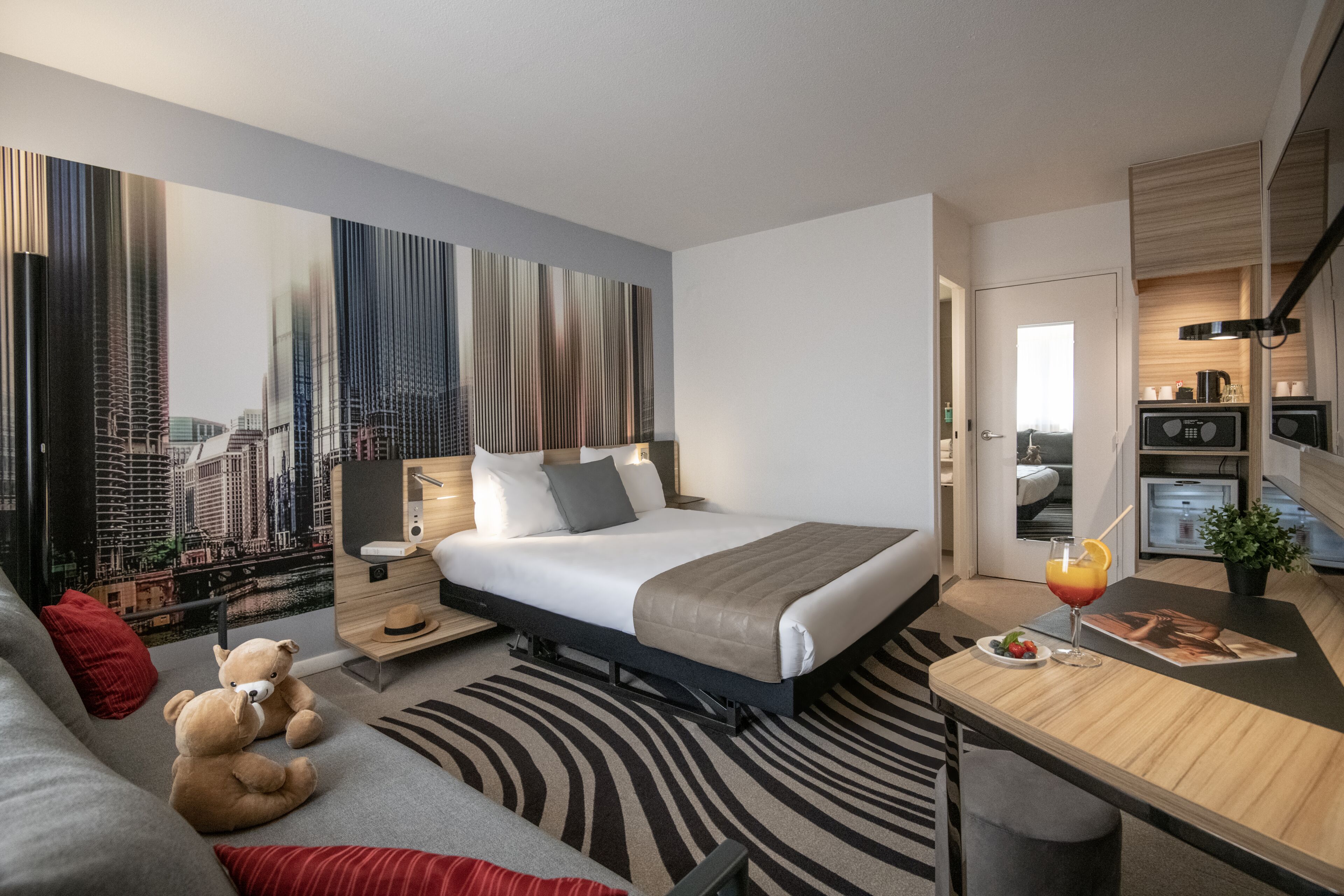 Een moderne hotelkamer met een groot bed, een bureau, een sofa en een teddybeer.