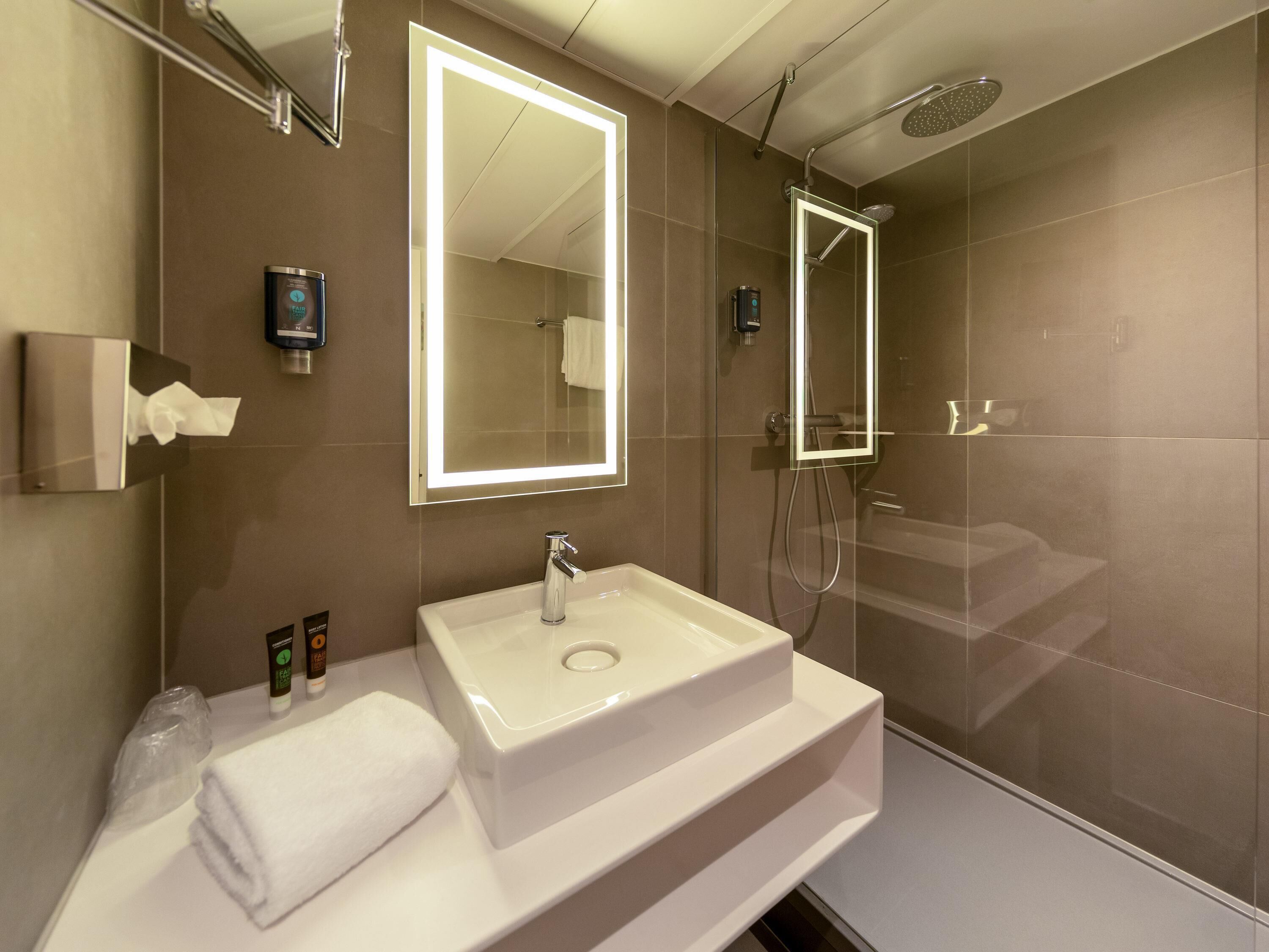 Une salle de bain moderne avec un grand miroir, un lavabo et une douche.