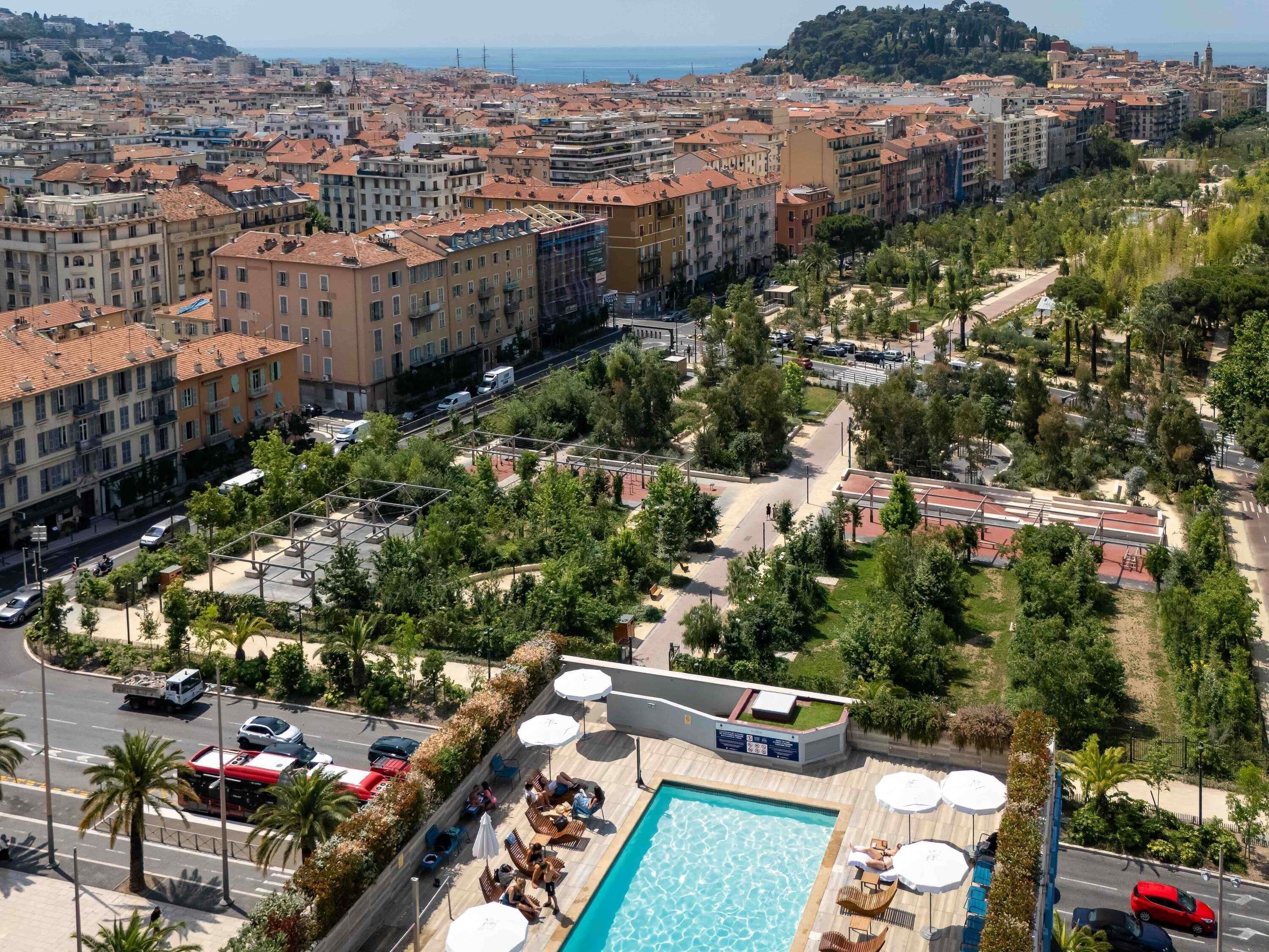 A rooftop pool area with lounge chairs and umbrellas, surrounded by trees and buildings.