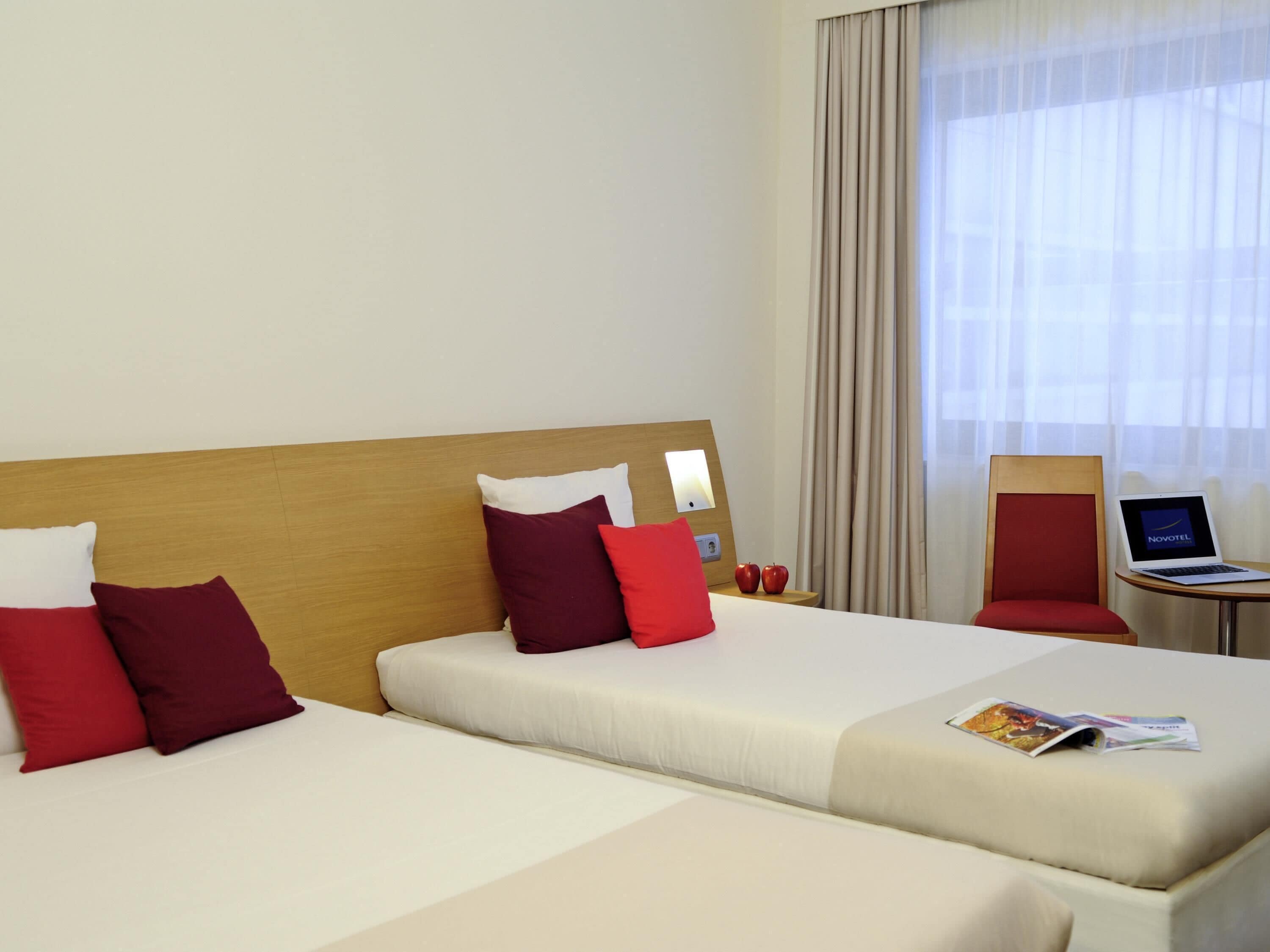 A hotel room with two beds, a laptop on a small table, and a view of the outside through the window.