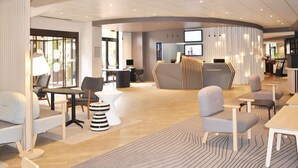 Een moderne hotel lobby met een receptiebalie, een zithoek en een groot scherm.