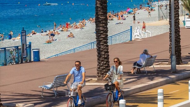 Een kustpromenade met palmbomen, een strand en een stadsbeeld op de achtergrond.