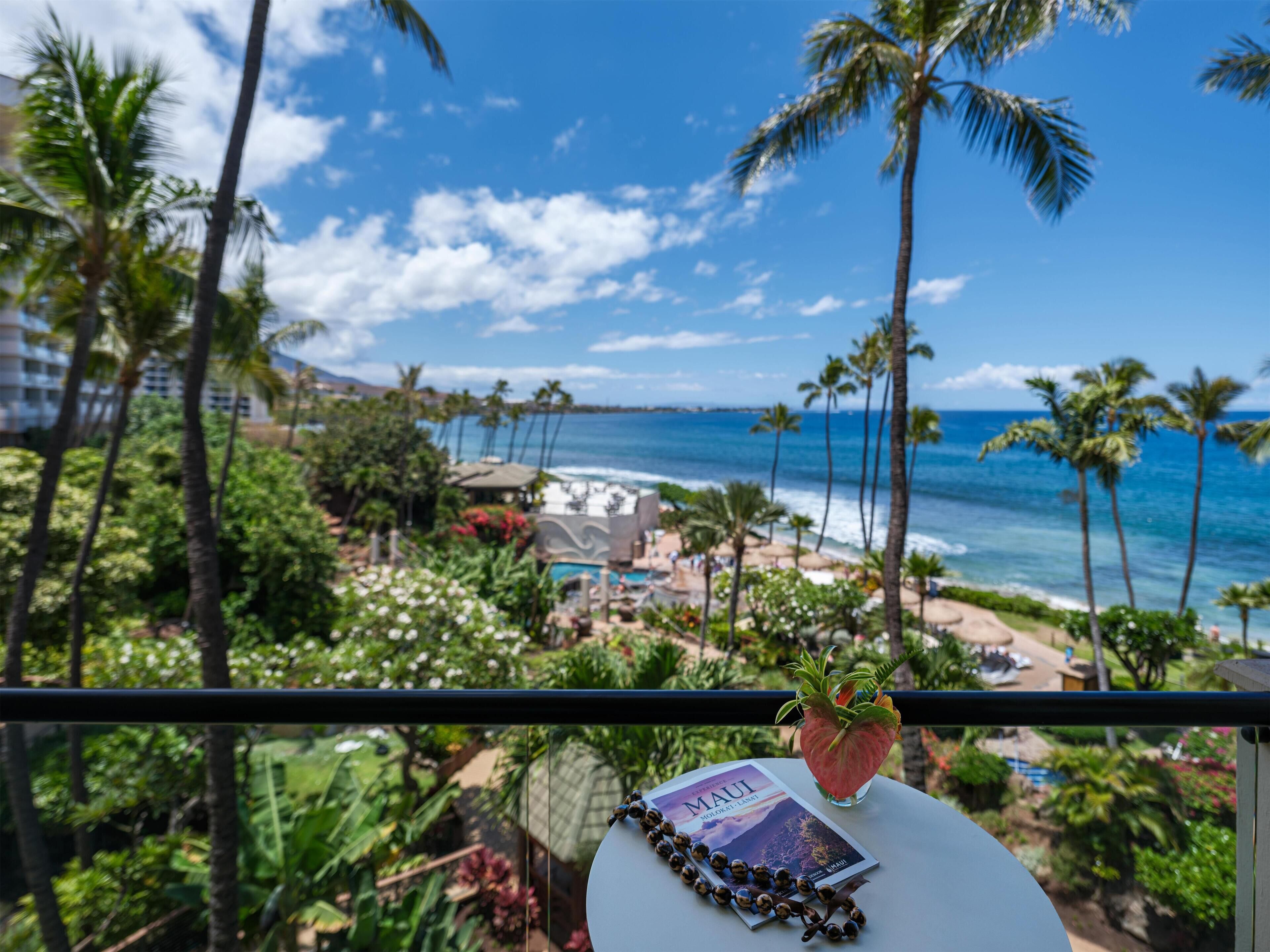 A balcony with a view of a beach, palm trees, and a book titled 'Maui.'