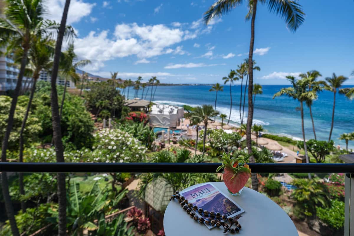 A balcony with a view of a beach, palm trees, and a book titled 'Maui.'