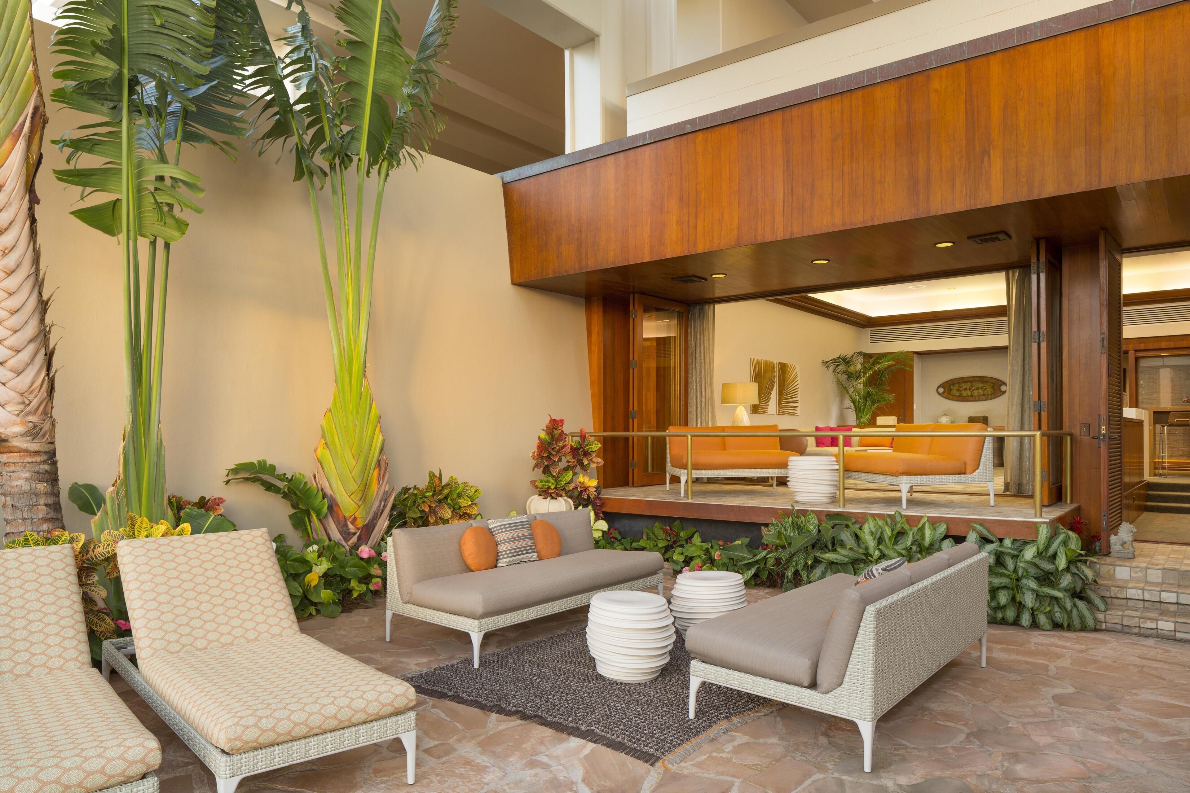 An outdoor seating area with wicker furniture, a stone floor, and tropical plants.