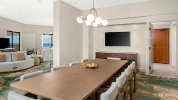 Une chambre d’hôtel moderne dotée d’une grande table à manger, de sièges confortables, d’un téléviseur à écran plat et offrant une vue sur l’océan.
