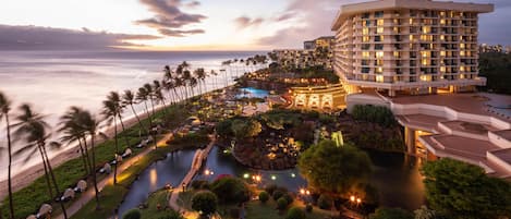 Un resort con piscina, palmeras y vista al océano al atardecer.
