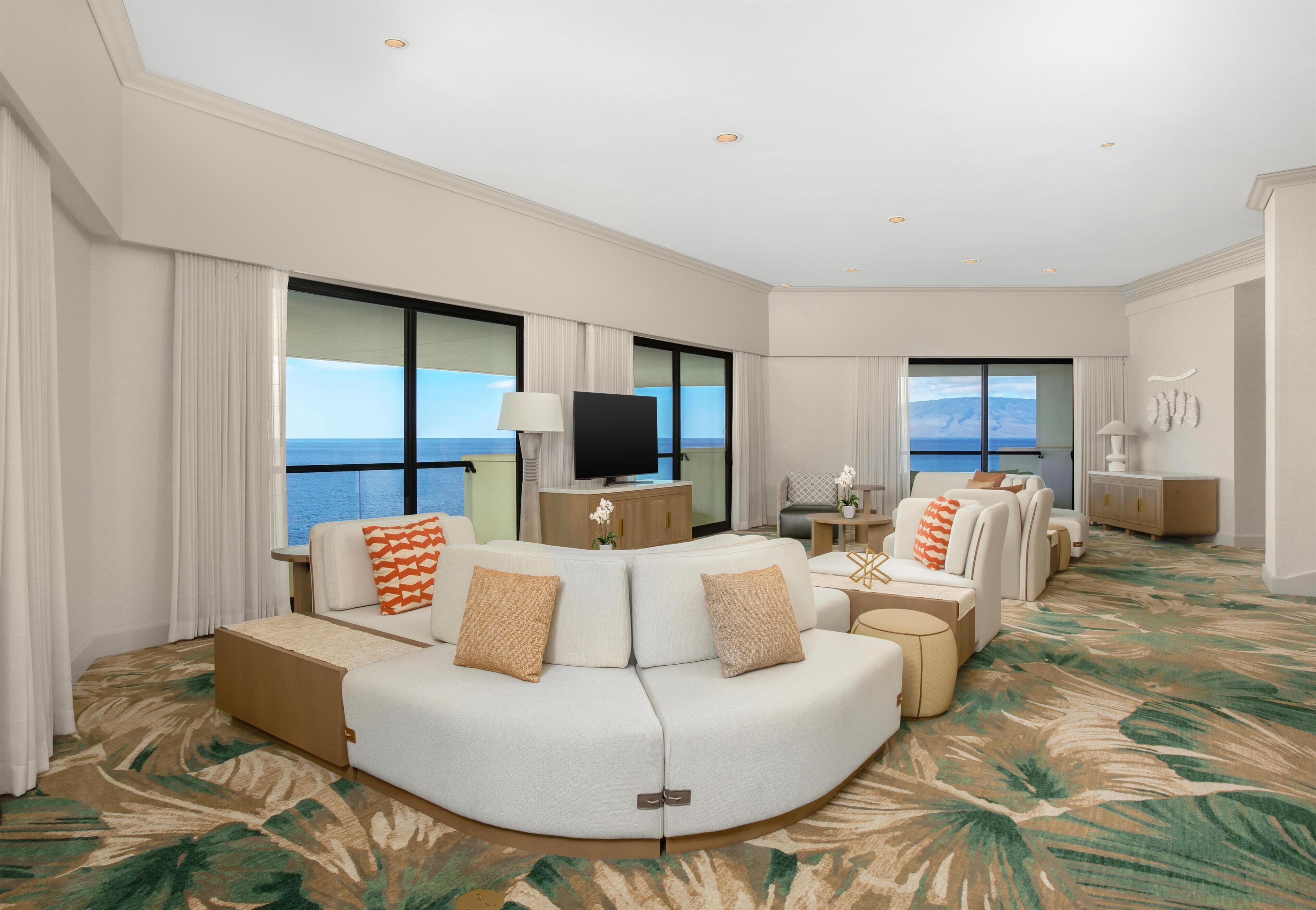 A hotel room with a curved sofa, a television, and large windows offering a view of the sea.