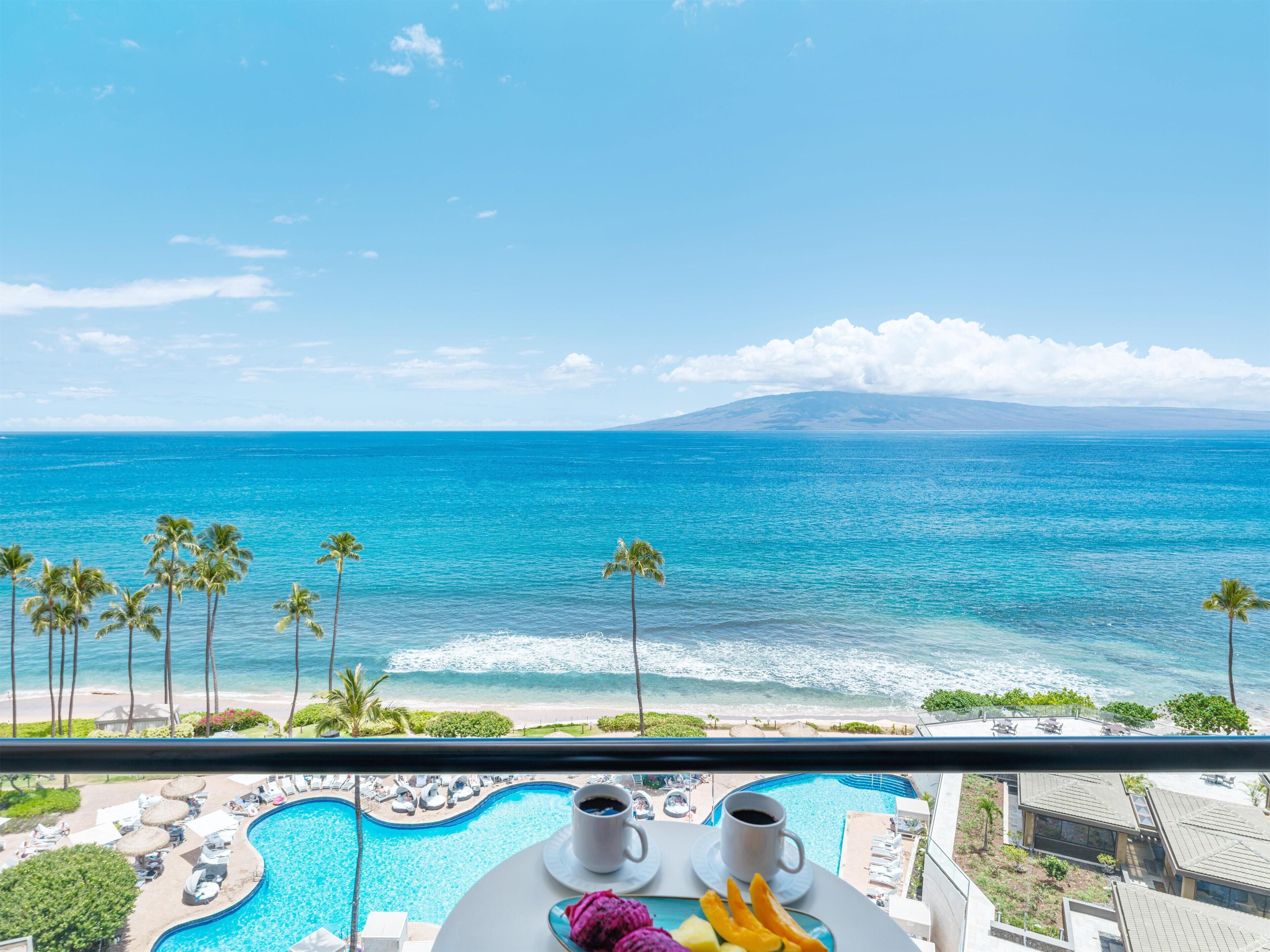 A poolside view with a clear ocean view, a beach, and a mountain in the distance.