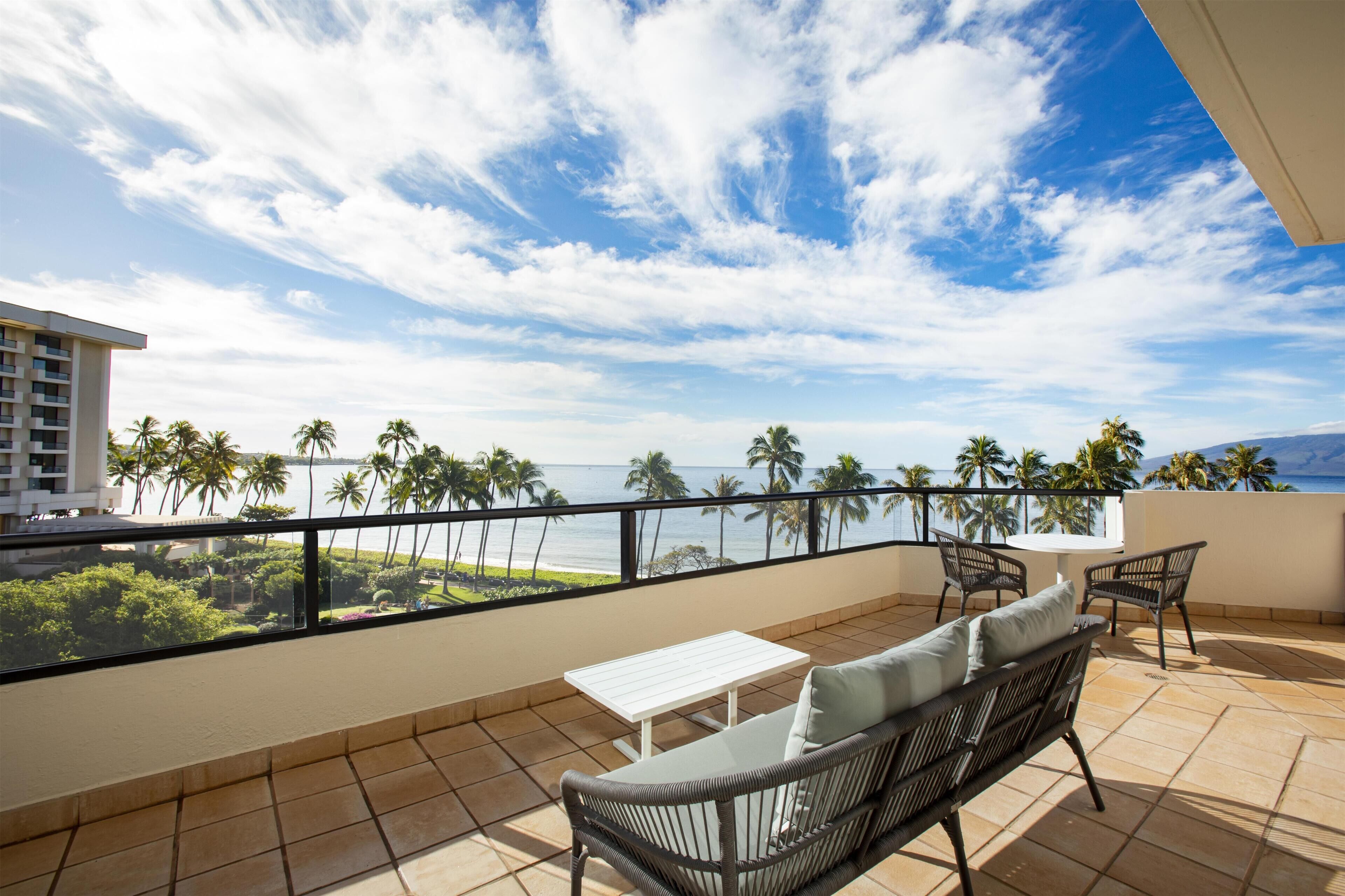 A balcony with a view of the ocean, a white table, and two wicker chairs.