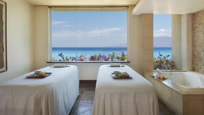 A room with two beds, a bathtub, and a large window with a view of the sea.