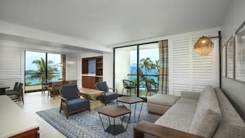 Una sala de estar moderna con sofá, sillas, una mesa de centro y una zona de comedor con vista al océano.