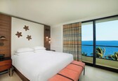 A bedroom with a large bed, a nightstand, a bench, and a view of the ocean.